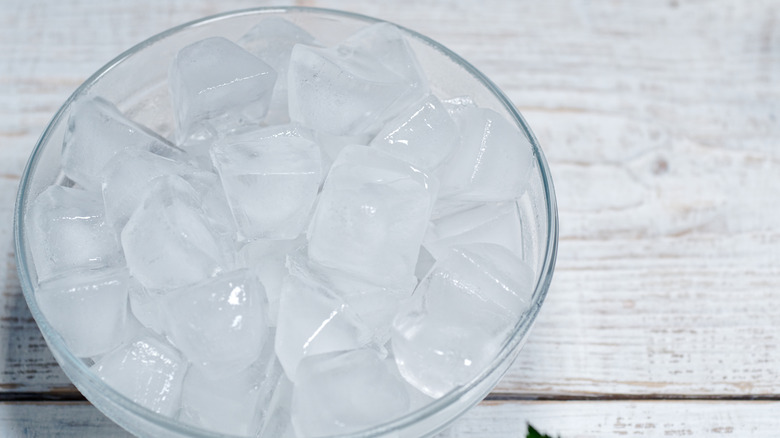 Ice cubes sit in a glass bowl on a wooden table