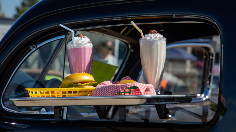 Milkshakes and a burger sit on a tray affixed to a car window