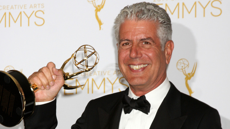 Anthony Bourdain in a tuxedo holding an Emmy Award in front of a white Emmy's promotional background