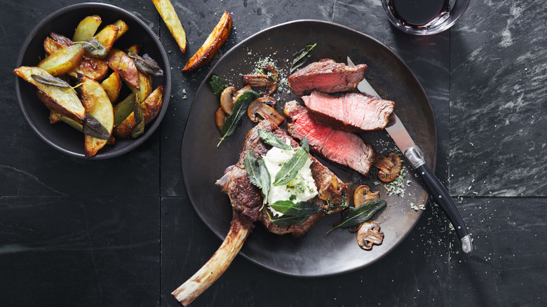 Steak topped with cheese and herb garnish with potato wedges