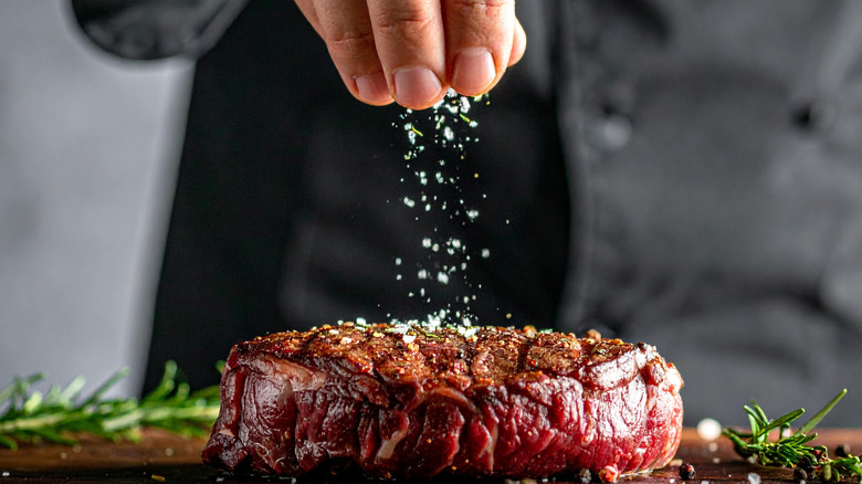 A chef seasoning a steak