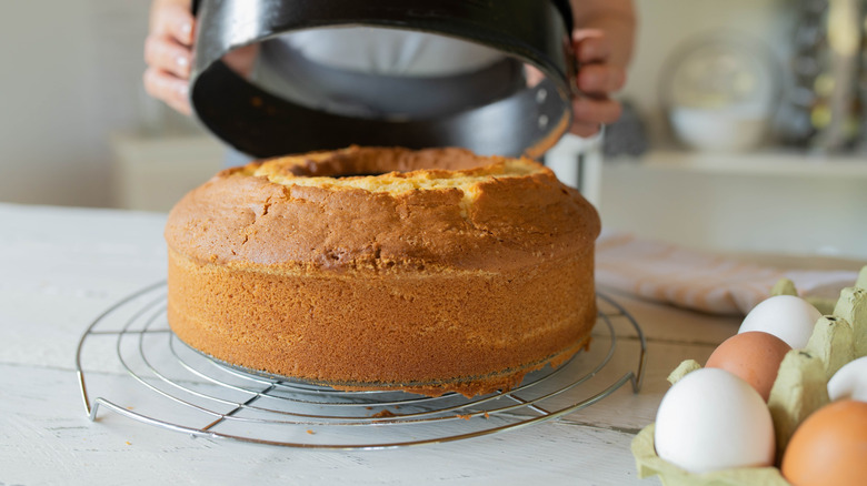 A woman uses both hands to remove the pan from a bundt cake that rests on a metal rack