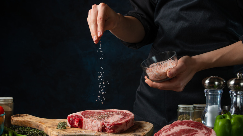 salt being sprinkled onto steak on a wooden cutting board