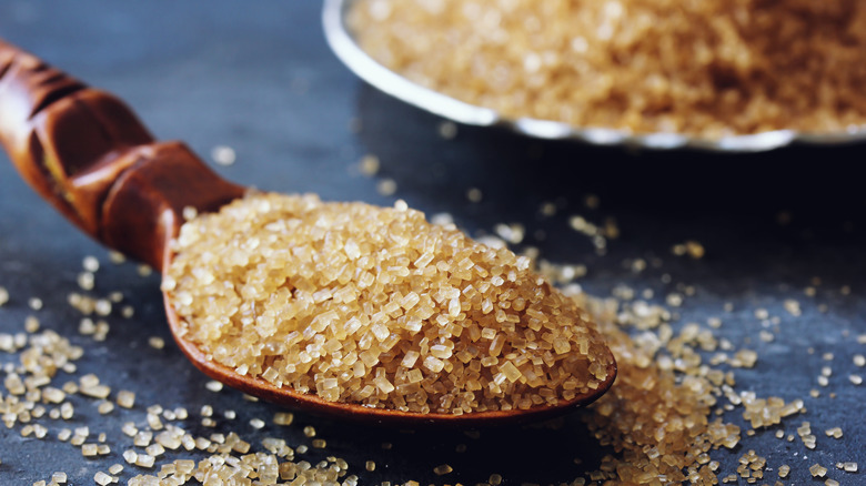Close of turbinado raw sugar crystals in a wooden spoon