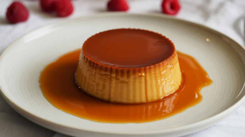 flan on a plate with raspberries in the background