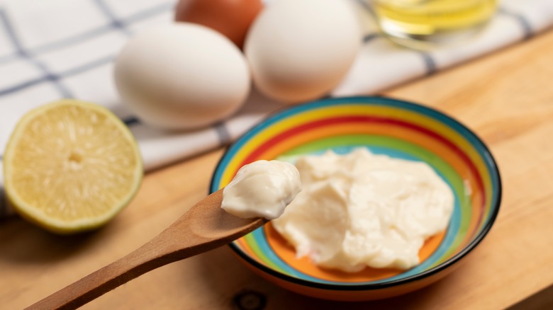Spoonful of mayonnaise surrounded by bowl of mayo and mayo ingredients