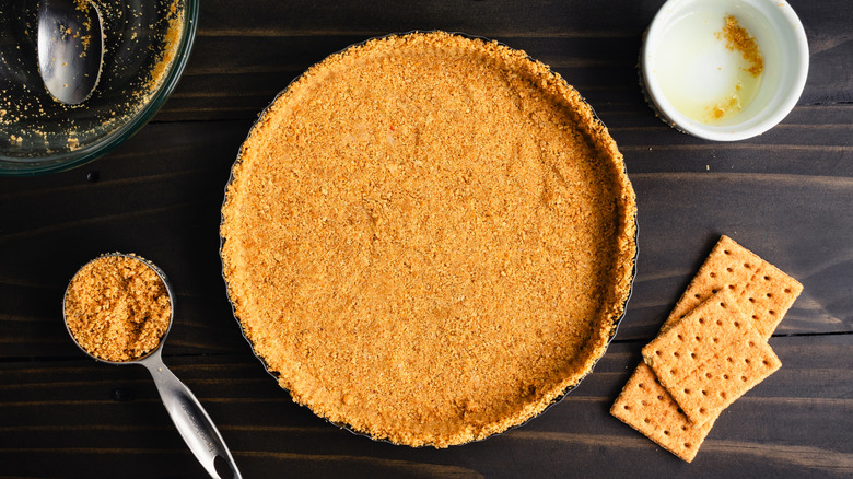Unbaked graham cracker crust in a tart pan: Freshly made graham cracker crumb crust surrounded with kitchen tools and extra ingredients