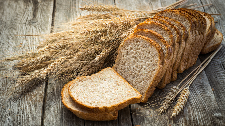 Sliced wheat bread on wood next to wheat