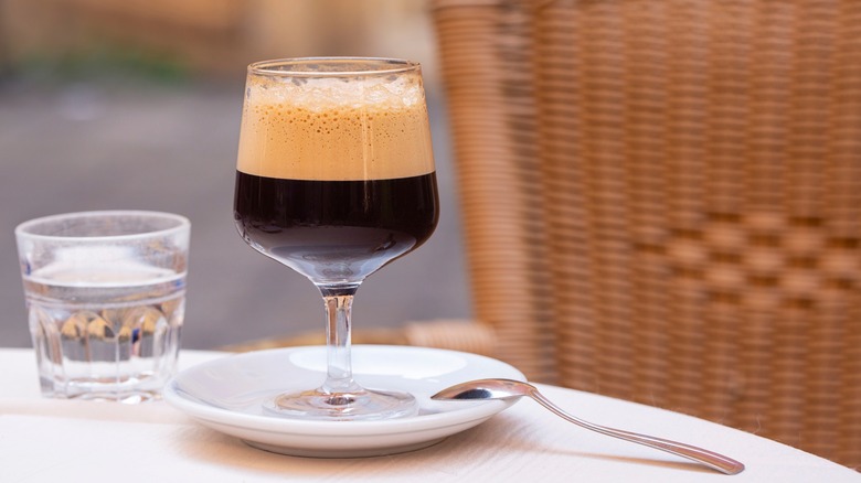 A shakerato coffee drink sits on a table next to a glass of water.