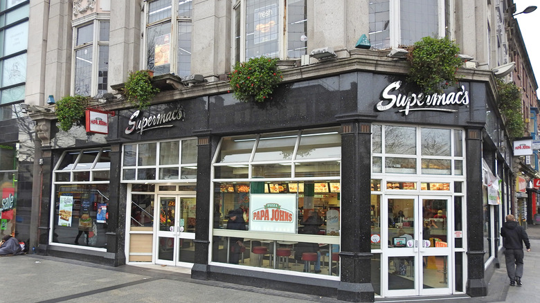 Supermac's fast food restaurant on the corner of a street in Dublin, Ireland with a dark exterior and light doors, attached to a larger building complex.