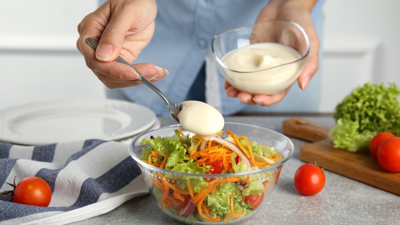 Hands adding mayonnaise to salad