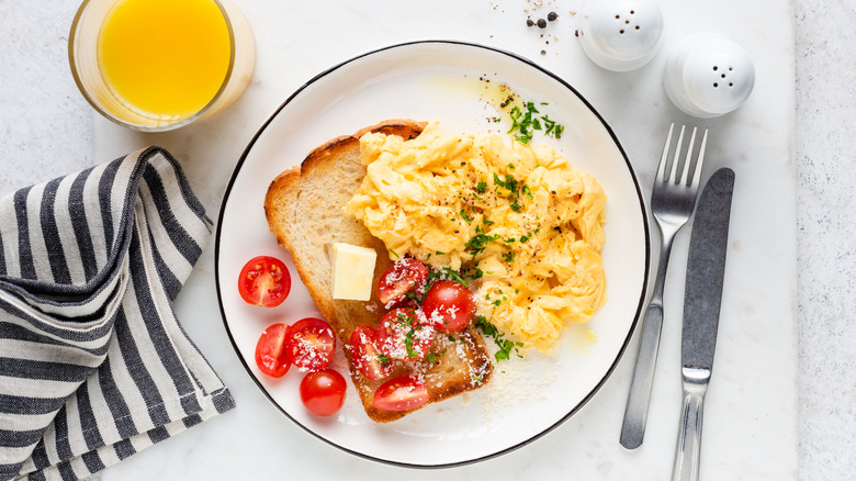 A glass of orange juice next to a plate of scrambled eggs and toast