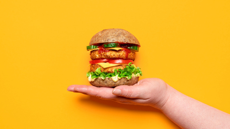 A hand holding a homemade vegan burger on an orange background.