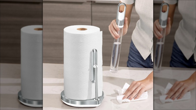 A simplehuman Paper Towel Holder sits on a counter as a woman uses the spray cleaner attachment