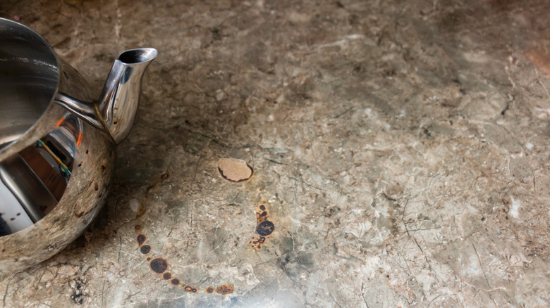 A teapot sits next to heat damage and scorch marks on a laminate countertop