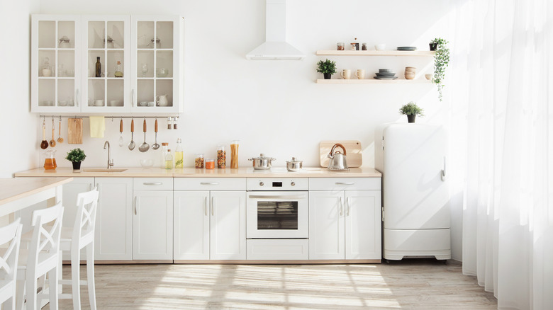 A bright kitchen with light-colored floors and white walls, cupboards, appliances, and decor