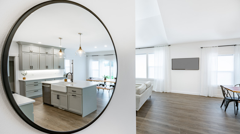 A black-framed round mirror shows a kitchen in its reflection