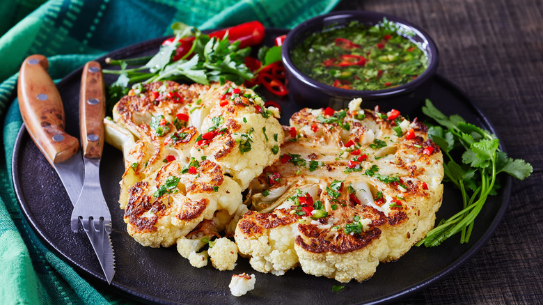 Cauliflower steaks with herbs and chili on black place with fork and knife