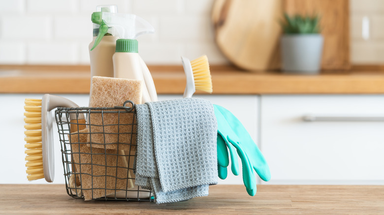 A variety of cleaning products in a basket rest on a kitchen counter.