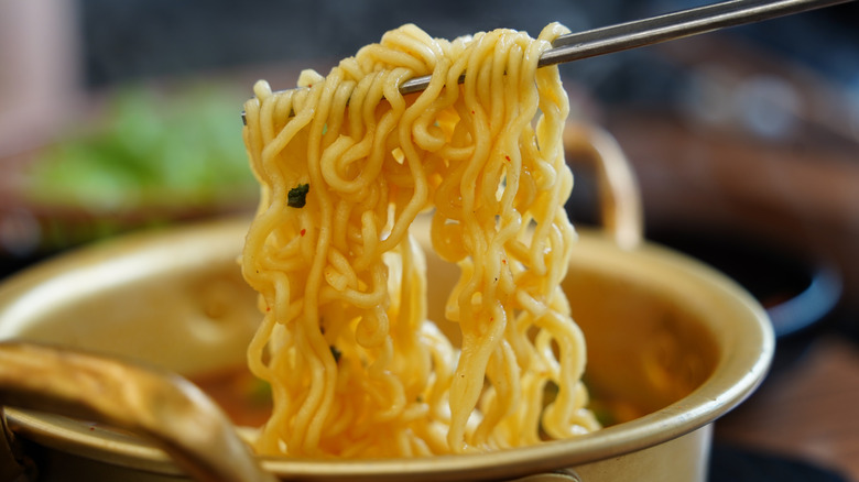 Chopsticks lifting cooked ramen noodles from a pot.