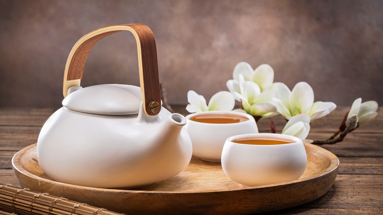 A teapot with two cups of tea and flowers