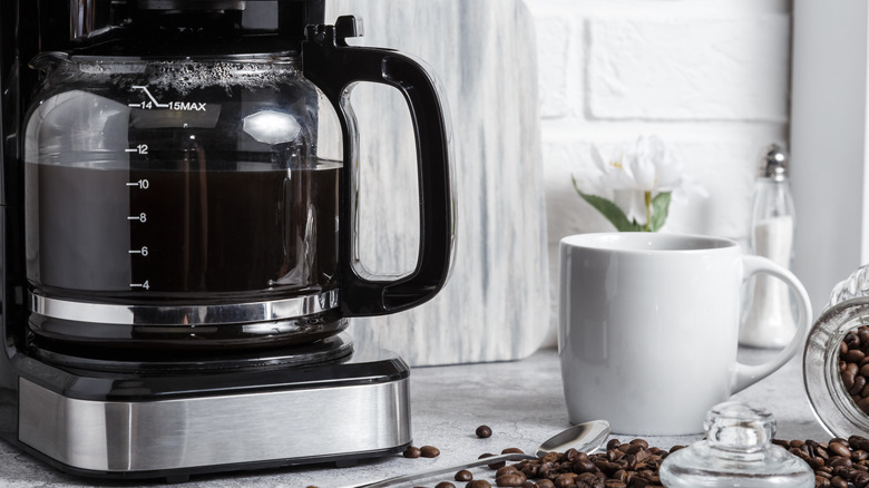 A coffee mug sits next to a full coffee maker.