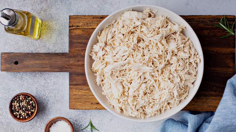 Shredded chicken sits in a large white bowl on a wooden cutting board
