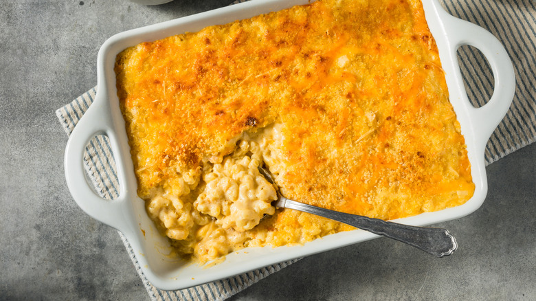 A spoon scoops mac and cheese from a casserole dish