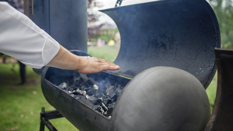 A hand checks the heat on a smoker.
