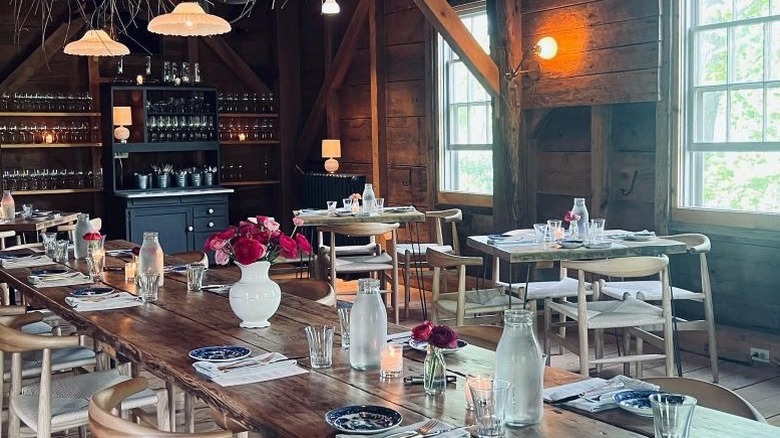Rustic restaurant dining room with one long table and chairs and two smaller square tables in the background