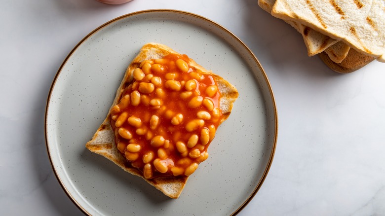 Beans on toast served on a plate with stack of toasted bread in background
