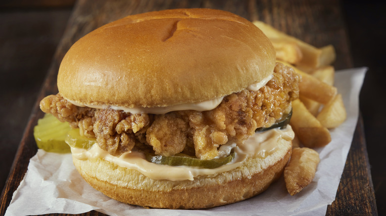 fried chicken sandwich with pickles and hot sauce next to fries