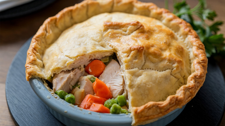A chicken pot pie rests in a pan, with a slice of top crust removed to expose the chicken and vegetables within