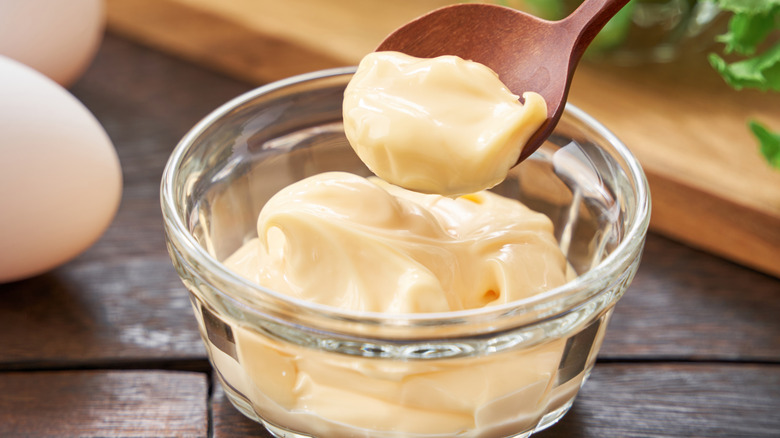 A glass bowl and wooden spoon full of mayonnaise