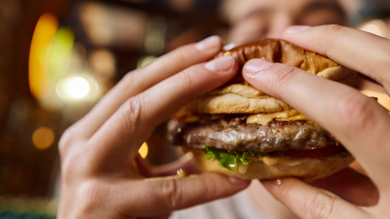 Two hands hold up a cheeseburger