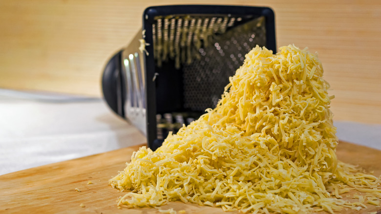 Pile of shredded cheese next to box grater on its side