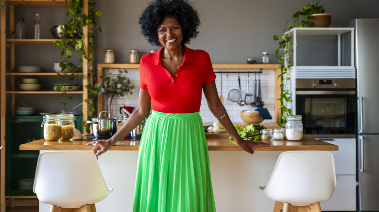 A homeowner in brightly colored clothes stands in a kitchen that has white elements as well as wood accents and pops of color