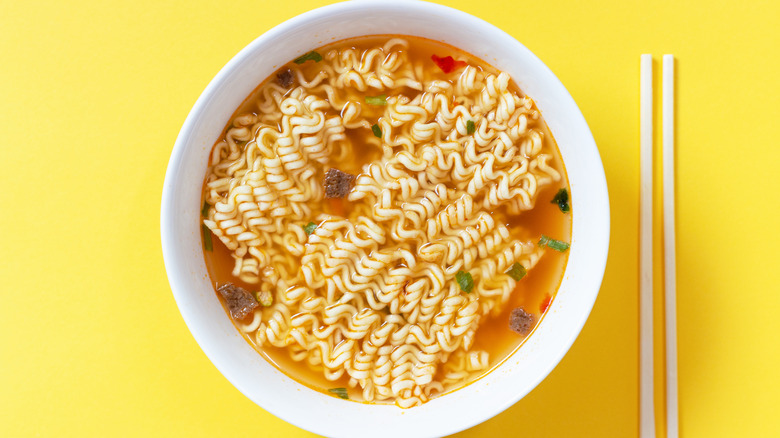 white bowl filled with ramen soup on yellow background; chopsticks on the side