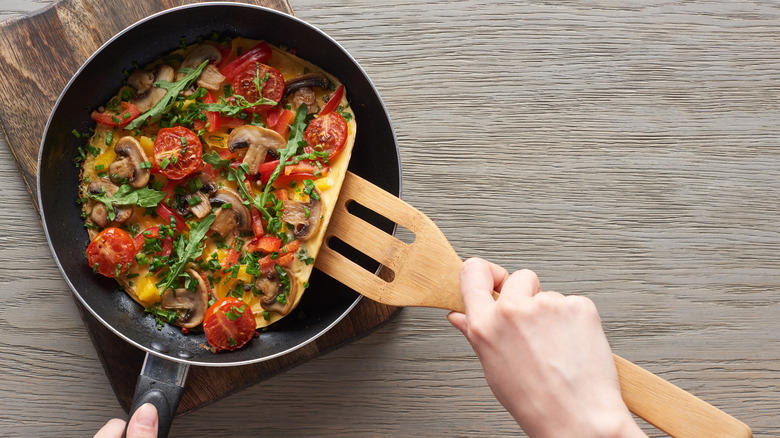 Omelet with mushrooms, tomatoes and chives in pan.