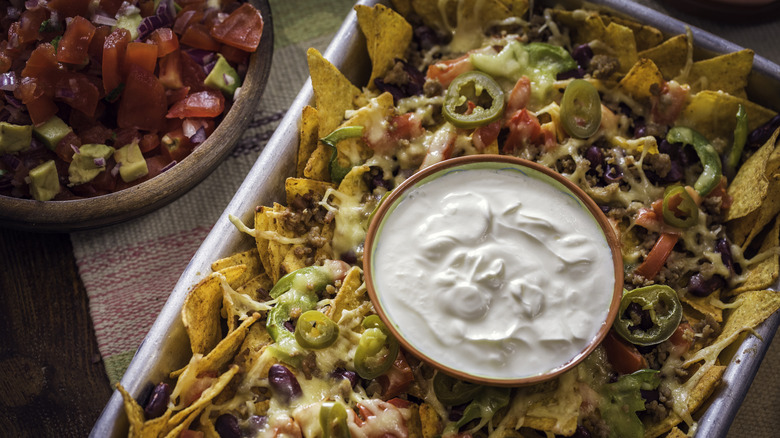 Tray of nachos with a bowl of sour cream on top and pico on the side