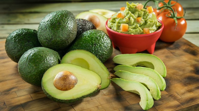 Pile of avocados next to bowl of guacamole