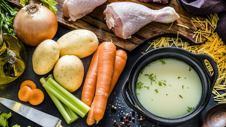 Ingredients for chicken rice soup surrounding a bowl of broth