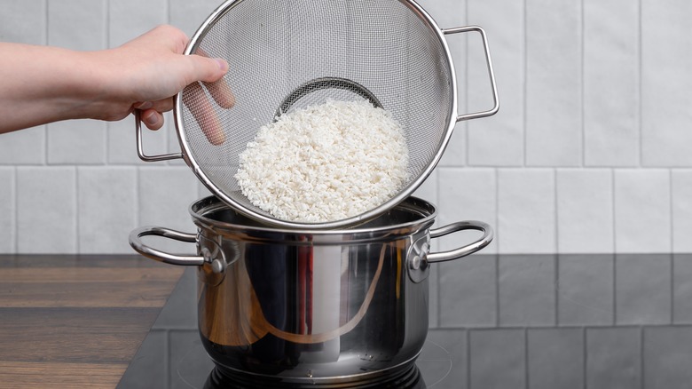Hand adding white rice to pot on stove