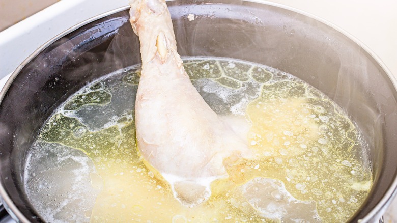 Chicken cooking in pot of water with fat on surface