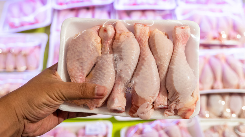 Hand holding package of raw chicken legs