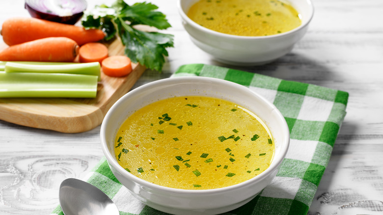 Bowl of seasoned chicken broth with veggies in background