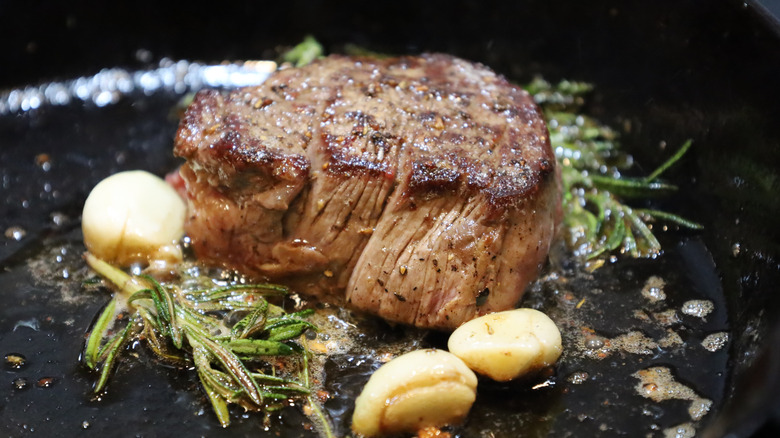 Steak cooking in pan with butter, garlic, and rosemary