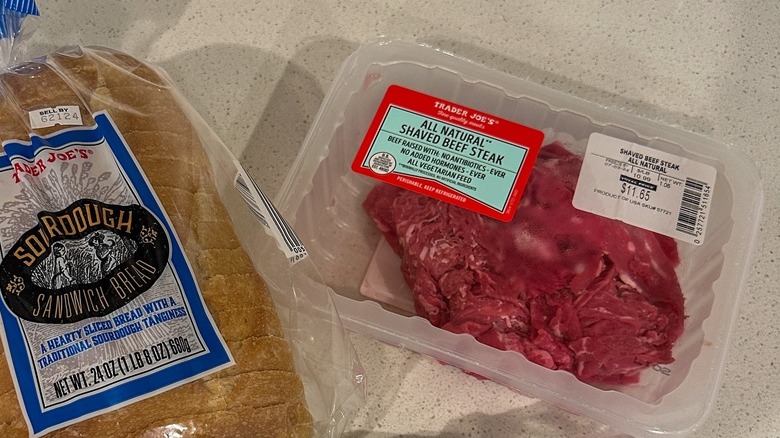 A package of Trader Joe's shaved steak sits next to a bag of sourdough bread on a counter
