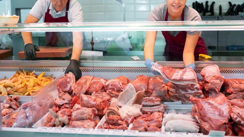 Two butchers reach into a refrigerated meat case