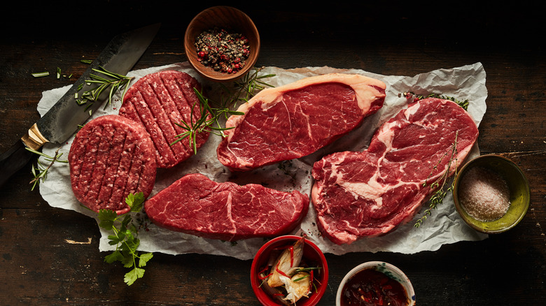 Assorted steaks on parchment paper with seasonings and herbs